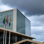 Fachada da CLDF com bandeiras LGBTQIAPN+ sob céu nublado, destacando falhas no combate à vulnerabilidade.