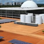 Fachada da Câmara Legislativa do DF em Brasília com elementos de hidrogênio e painéis solares sob céu nublado, destacando críticas ambientais.