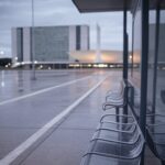 Parada de ônibus vazia em Brasília, DF, com arquitetura icônica ao fundo, representando cena de tragédia urbana.