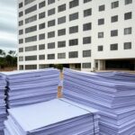 Fachada do Hospital de Base em Brasília com documentos de edital de licitação em primeiro plano, destacando priorização de preço sobre qualidade.