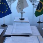 Mesa de assinatura do acordo histórico de livre-comércio entre UE e Mercosul em Brasília, com bandeiras e documentos oficiais.
