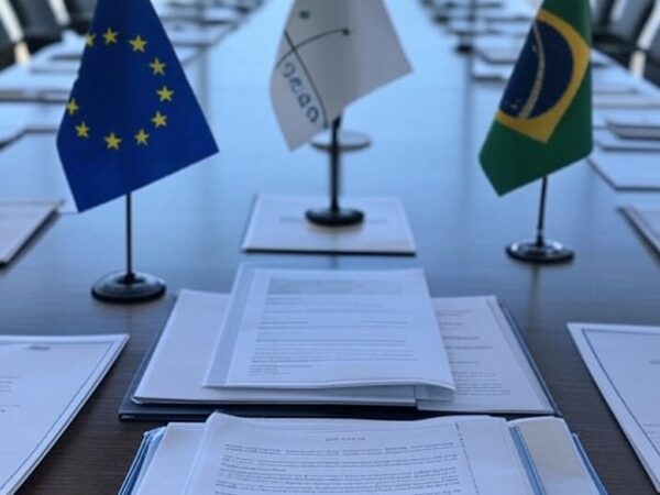 Mesa de assinatura do acordo histórico de livre-comércio entre UE e Mercosul em Brasília, com bandeiras e documentos oficiais.