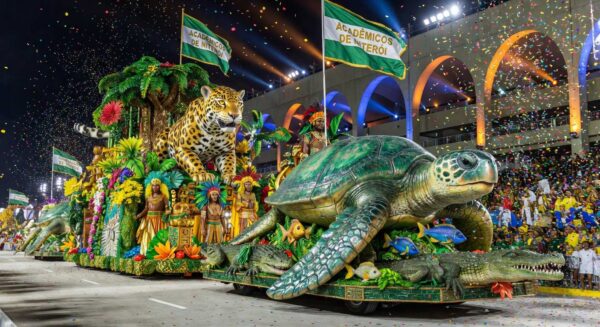 Desfile de carnaval no Sambódromo com carros alegóricos da Acadêmicos de Niterói, homenageando temas brasileiros, em ambiente festivo noturno.