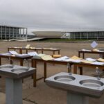 Mesa com pilhas de documentos burocráticos e carimbos em escritório de Brasília, representando aumento de burocracia em eventos.