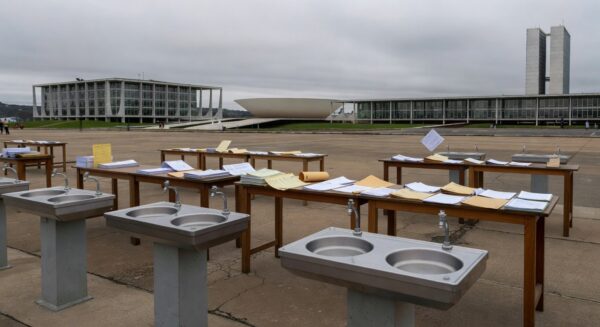 Mesa com pilhas de documentos burocráticos e carimbos em escritório de Brasília, representando aumento de burocracia em eventos.