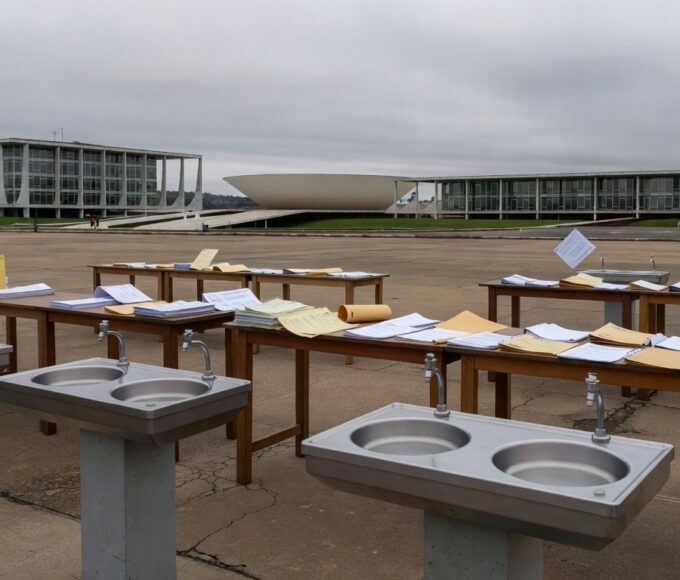 Mesa com pilhas de documentos burocráticos e carimbos em escritório de Brasília, representando aumento de burocracia em eventos.