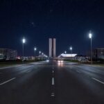 Avenida em Brasília iluminada por lâmpadas LED modernas à noite, com arquitetura da Esplanada dos Ministérios ao fundo.
