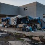Rua urbana brasileira com barracas improvisadas ao lado de prédio institucional
