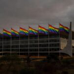 Fachada da CLDF em Brasília com bandeiras do arco-íris sob luz sombria, simbolizando discriminação